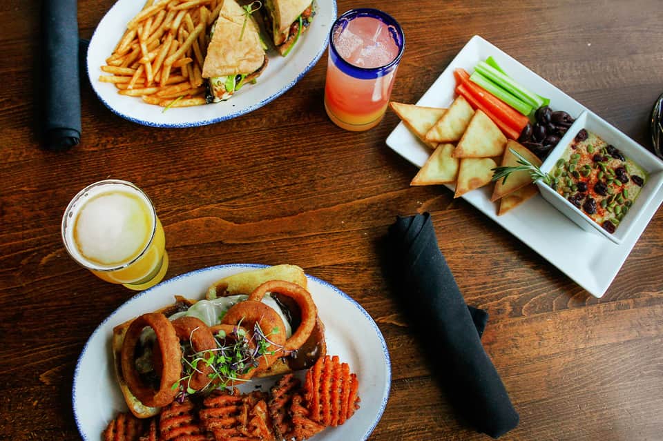 Gourmet lunch spread with cocktails, sandwich, onion rings, appetizers on wood table