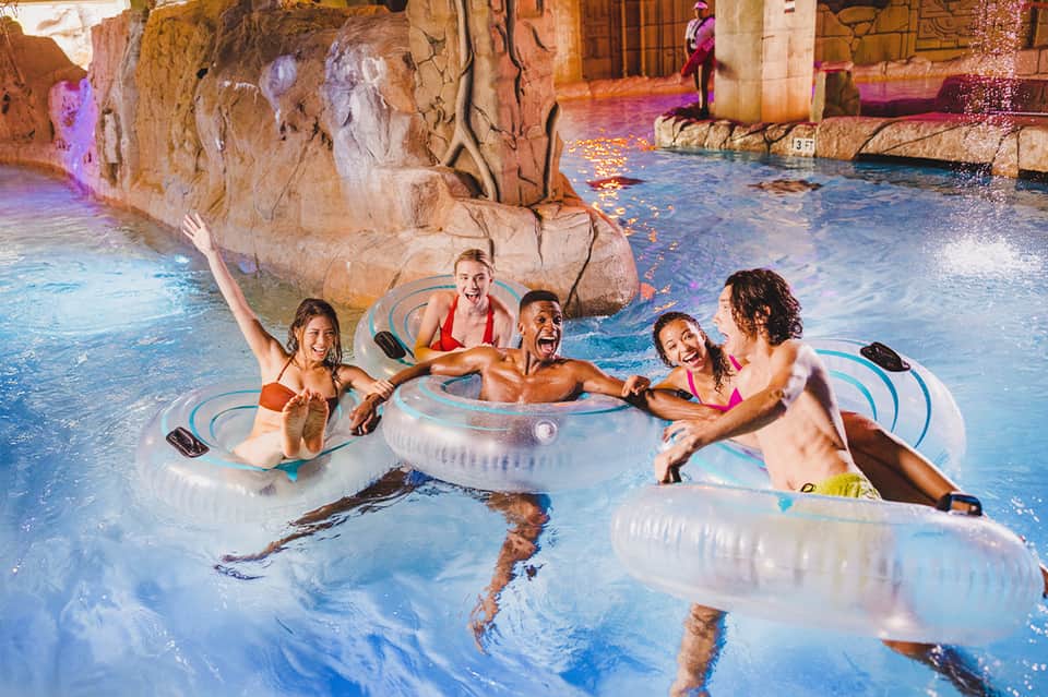 Children playing in themed indoor water park pool with colorful lighting and rock features
