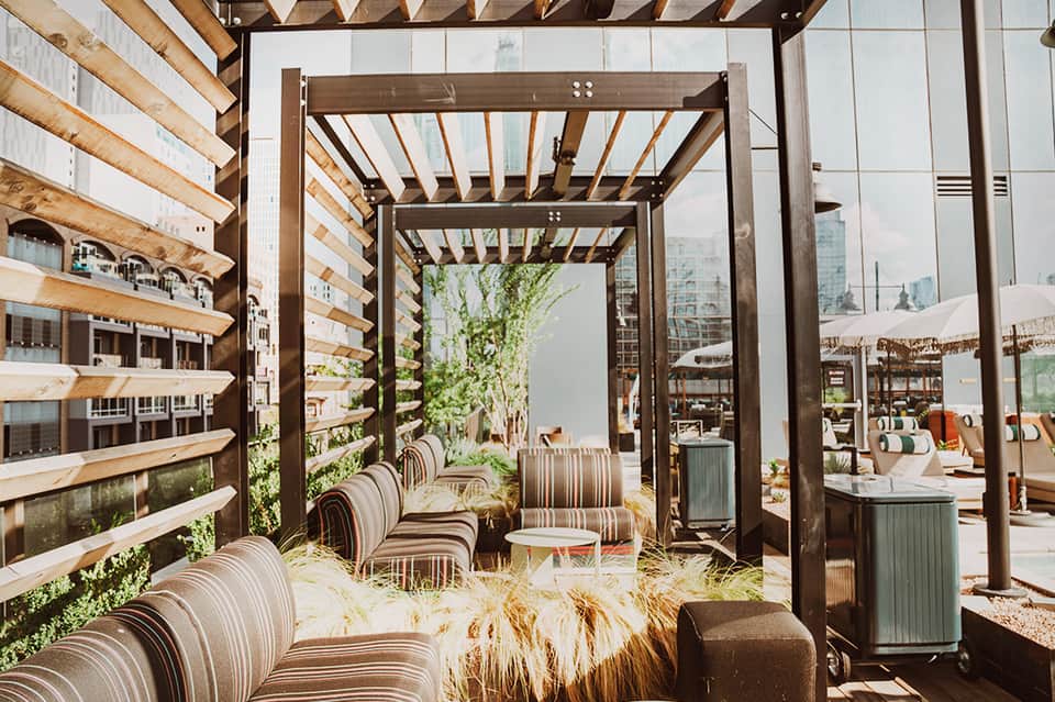 Modern rooftop lounge with wooden pergolas, striped chairs, city skyline views, and contemporary design