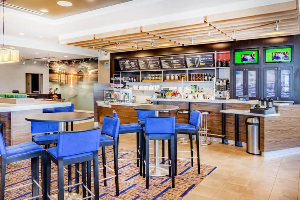 Hotel lounge with blue chairs, wooden ceiling beams, coffee bar, and TV displays