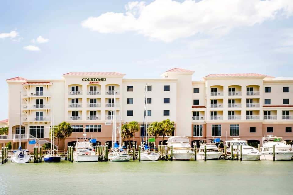 Waterfront Courtyard hotel with white and tan exterior, pink roof, docked boats, and palm trees
