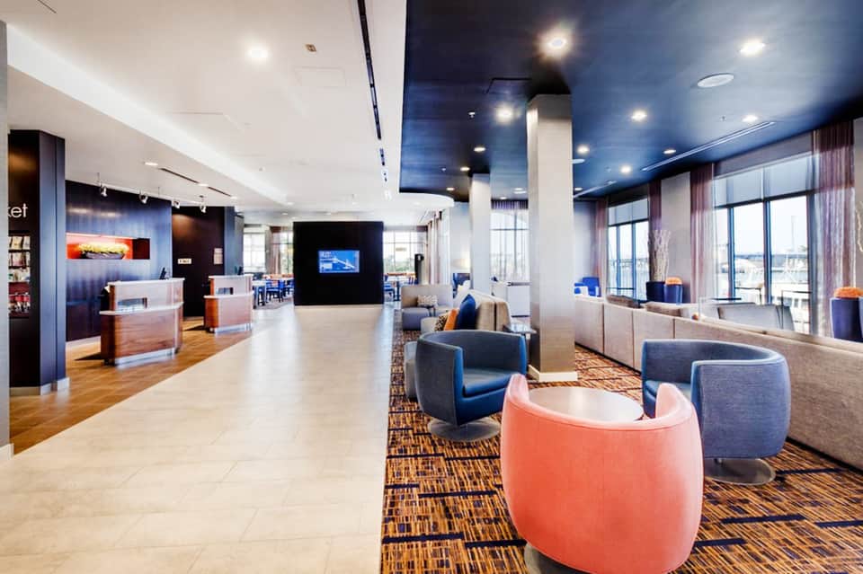 Modern hotel lobby with blue accents, coral seating, high ceilings, and floor-to-ceiling windows