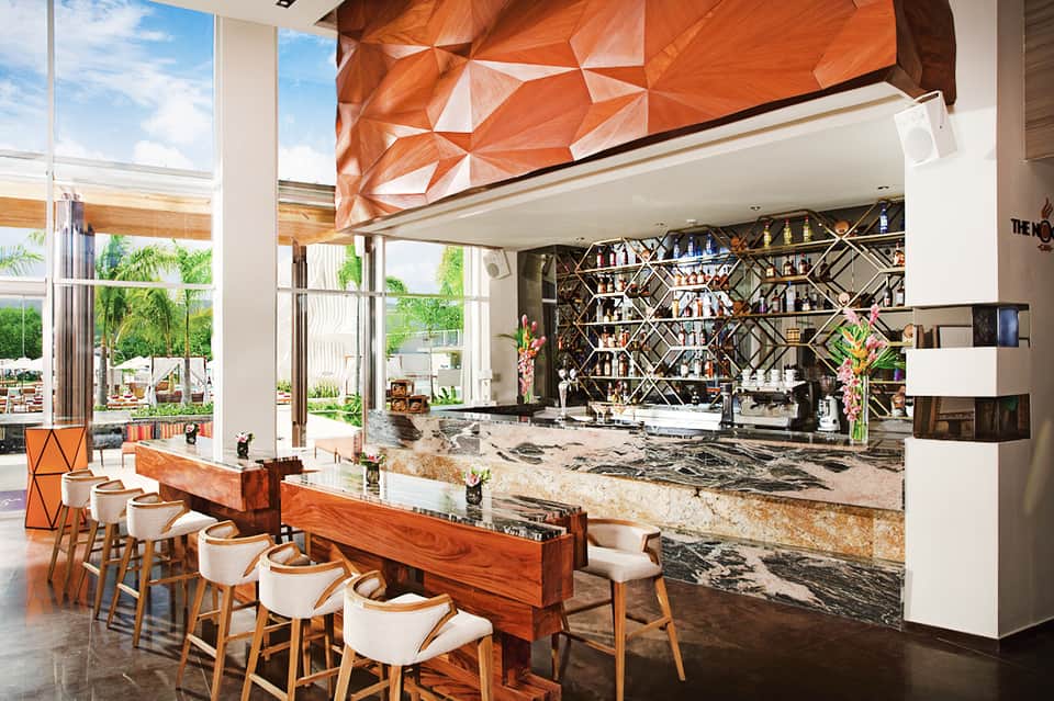 Modern resort bar with geometric orange ceiling, marble counters, and black lattice shelving