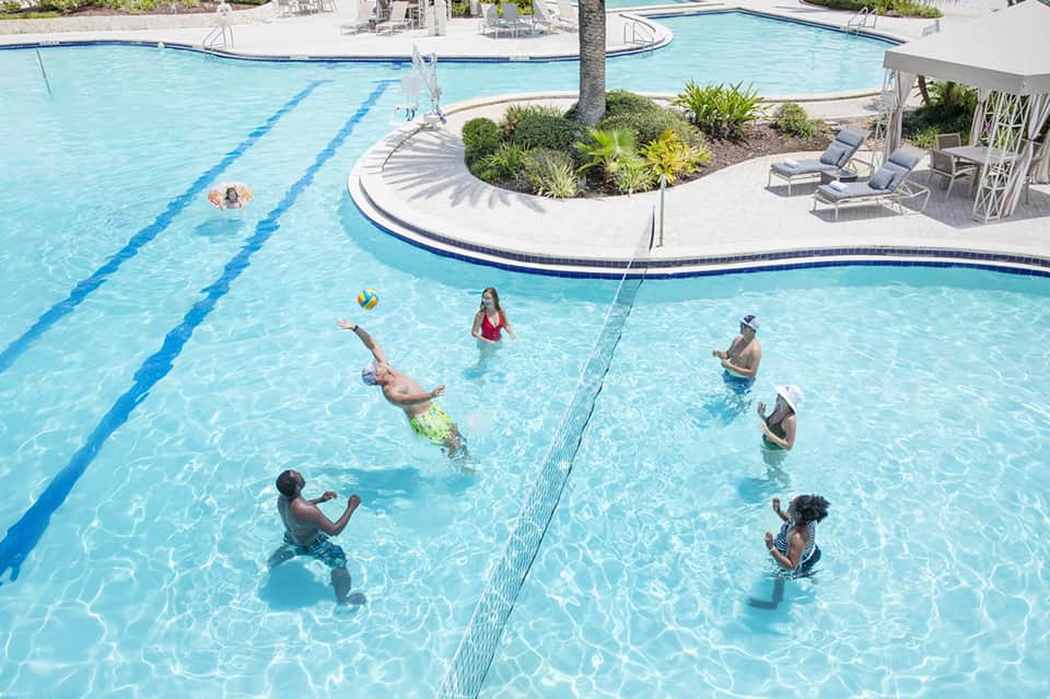 Resort pools with lap lanes and recreational areas, multiple swimmers, lounge chairs, and palm trees