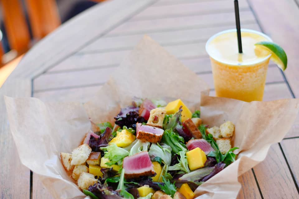 Colorful salad with seared tuna, greens, and croutons in paper wrapper with citrus cocktail on wooden deck