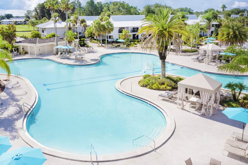 Aerial view of curved resort pool with white gazebo and palm tree landscaping