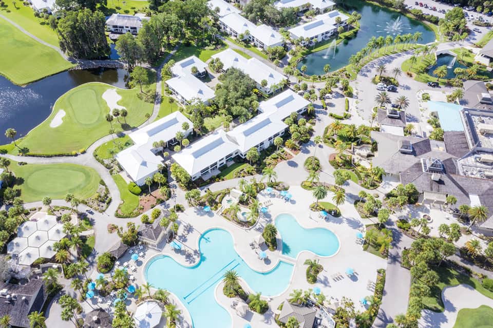 Aerial view of large resort complex with multiple pools, golf course, and lush tropical landscaping