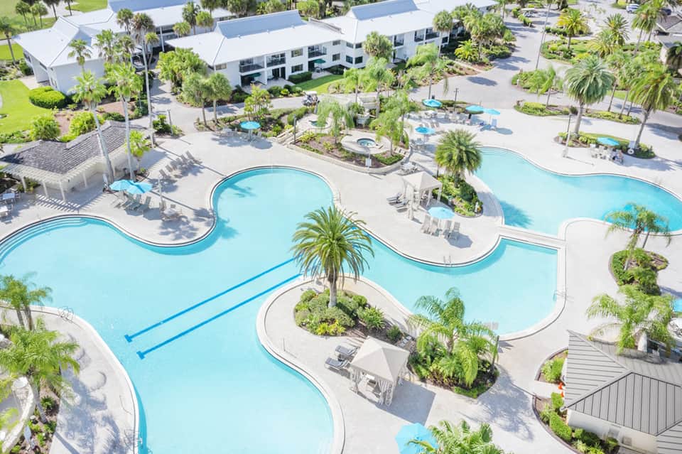 Aerial view of curved resort pools with palm trees, lounge chairs, and white buildings