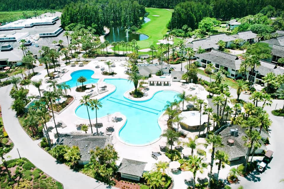 Aerial view of resort with curved blue pools, landscaped grounds, buildings, and golf course