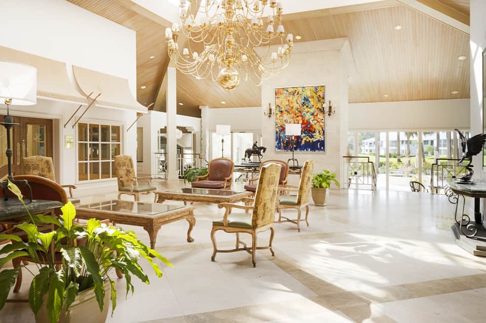 Elegant resort lobby with vaulted ceilings, crystal chandelier, tropical plants, and ocean views