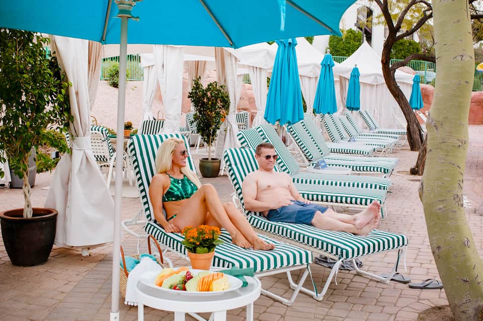 Guests relaxing on green and white striped lounge chairs under blue umbrellas with white curtained cabanas