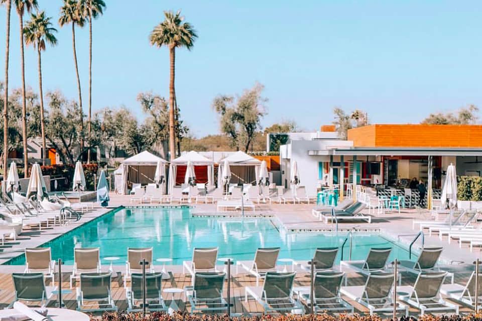 Resort pool with turquoise water, white loungers, cabanas, and palm trees under clear sky