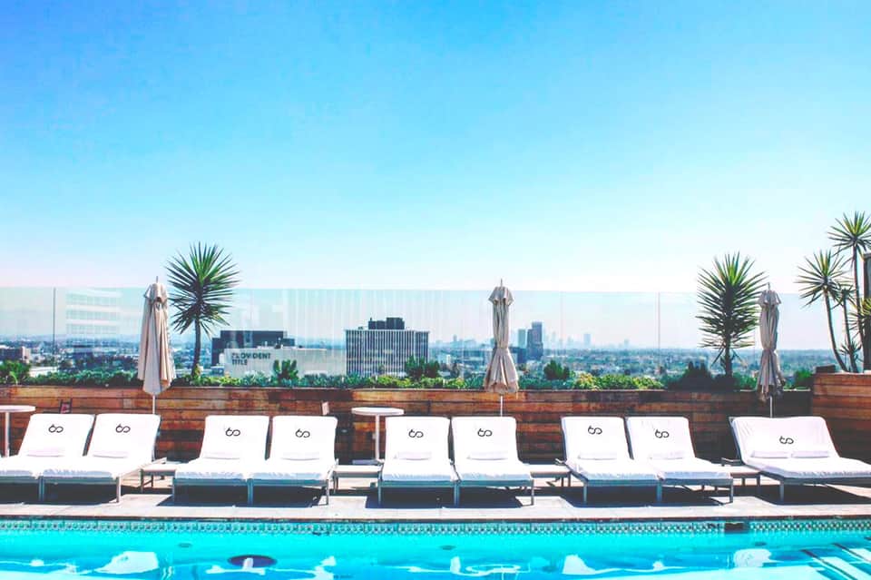 Luxury rooftop pool with white loungers and city skyline views under clear blue sky