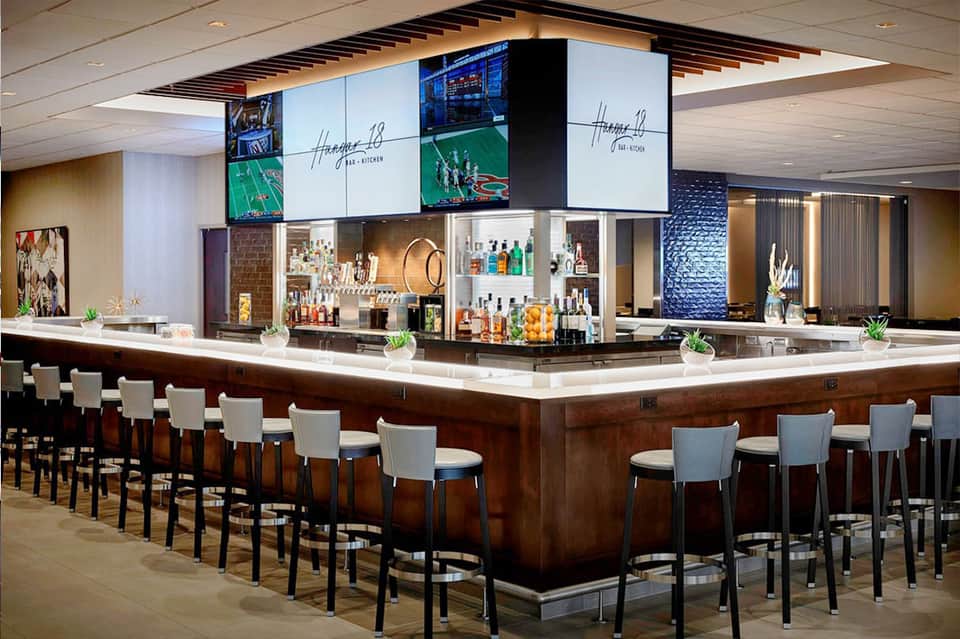 Modern hotel bar with dark wood counter, illuminated shelving, and black piano keys detail