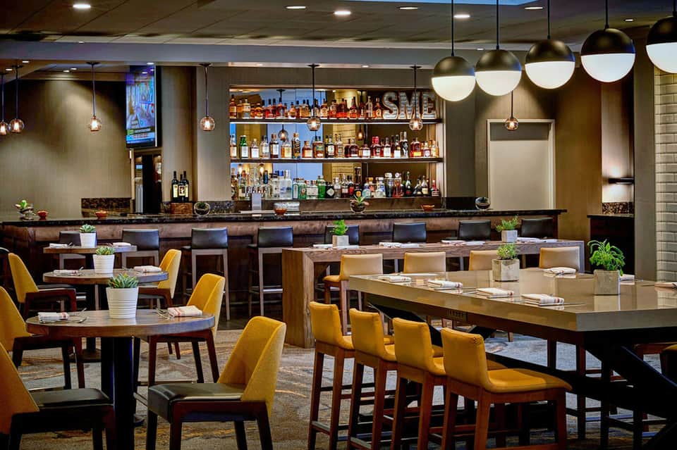 Modern hotel bar and lounge with full liquor selection, pendant lighting, and yellow chairs