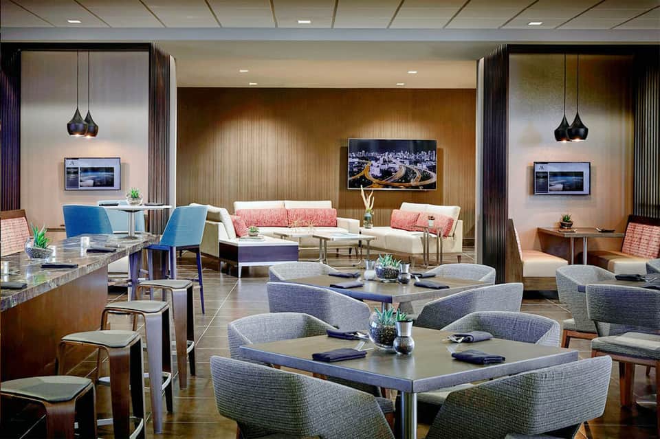 Upscale hotel lounge with modern furniture, coral accents, pendant lighting, and flat-screen TVs