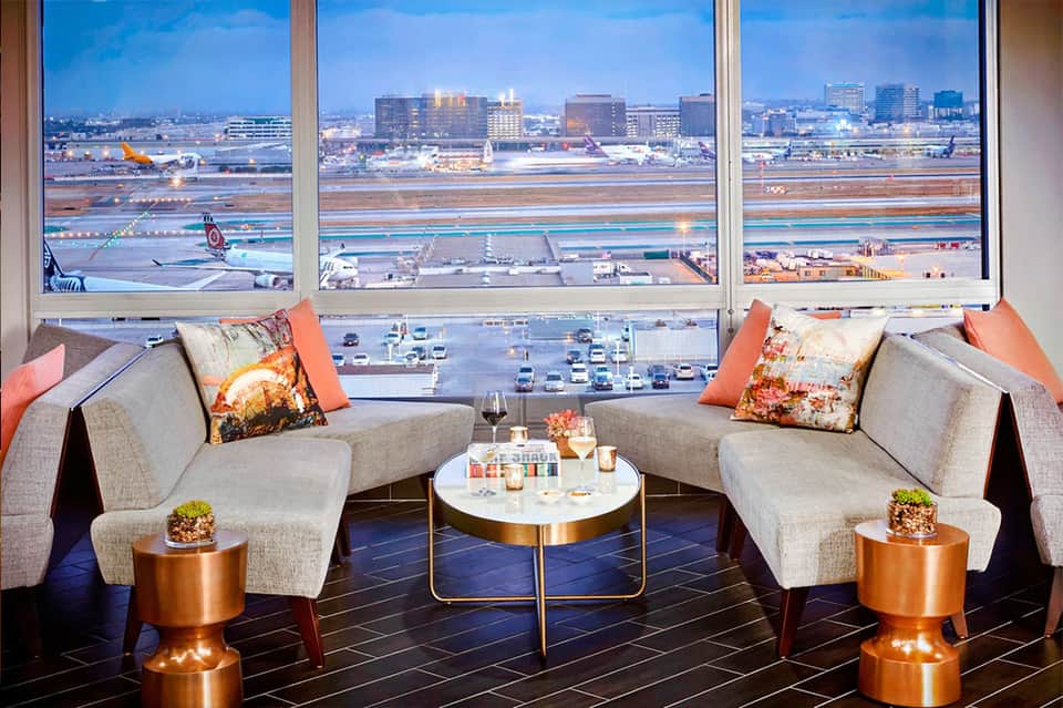 Airport lounge with gray seating, orange accents, and expansive runway views through windows