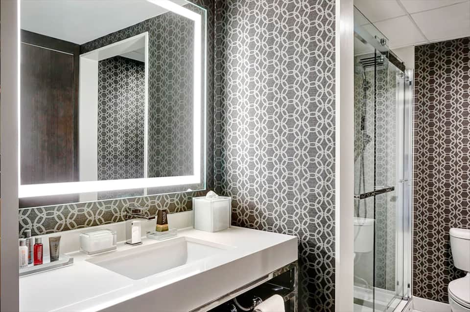 Modern bathroom with geometric patterned wallpaper, illuminated mirror, and glass shower