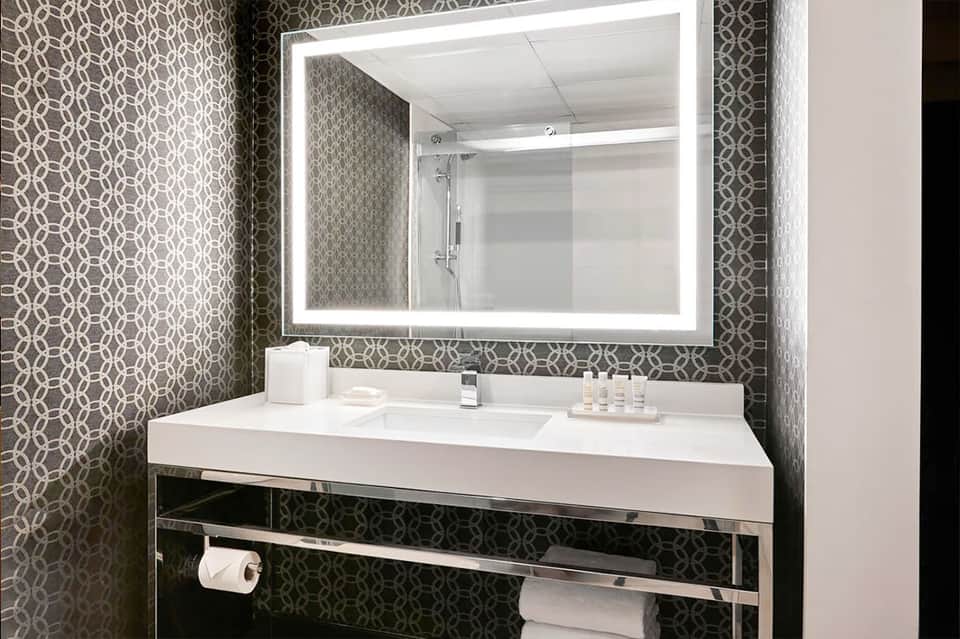 Contemporary bathroom with geometric patterned wallpaper, illuminated mirror, and white sink