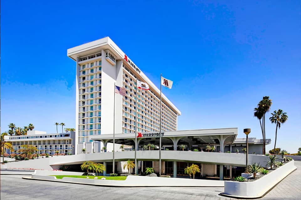 Beachfront Marriott hotel tower with white exterior, palm trees, clear blue sky, and curved architecture