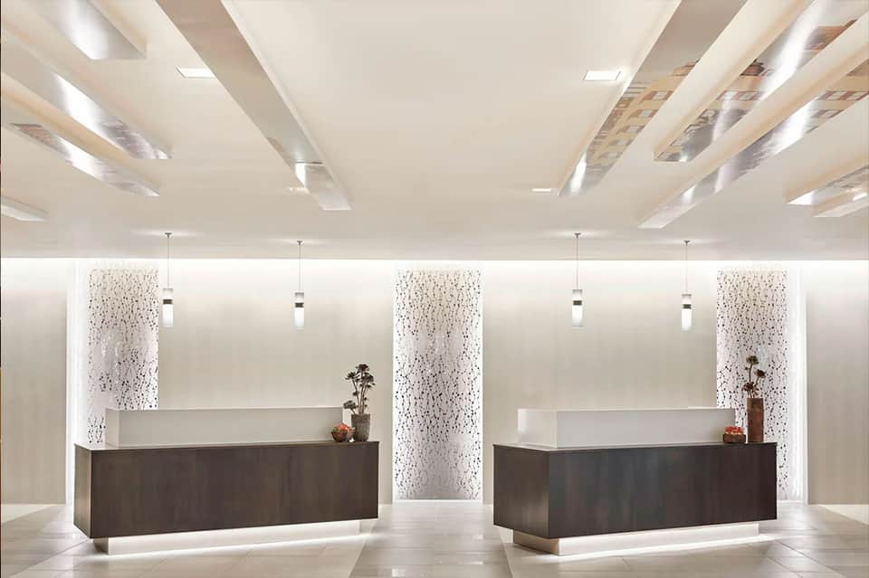 Modern hotel lobby with dual reception desks, dark wood counters, white walls, and pendant lighting