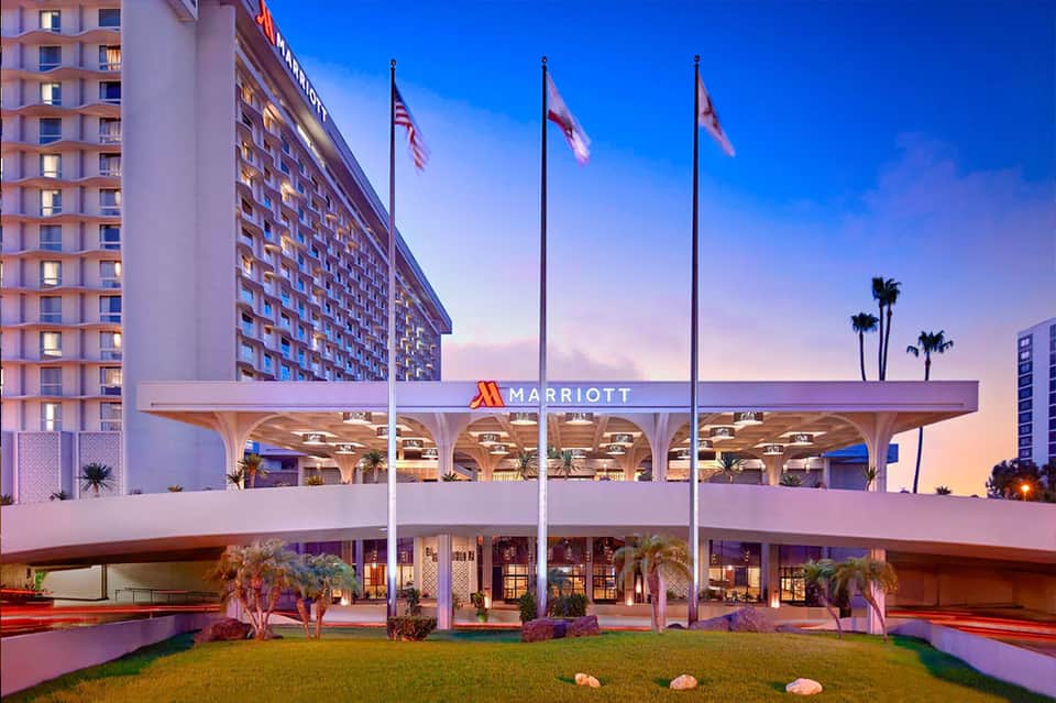 Marriott hotel entrance at dusk with pink lighting, flags, palm trees, and modern architectural canopy