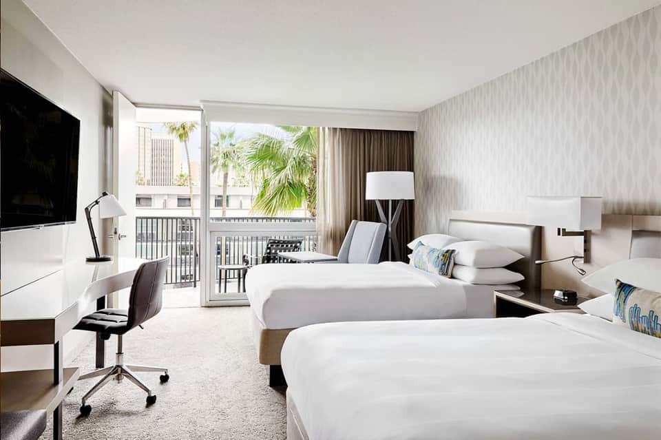Modern hotel bedroom with two queen beds, ocean-view balcony, flat-screen TV, and contemporary furnishings