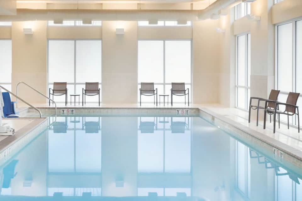 Bright indoor swimming pool with floor-to-ceiling windows and lounge chairs in a luxury hotel