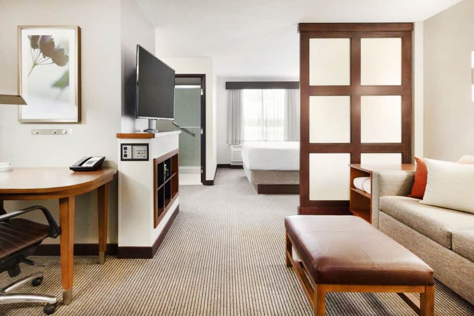 Modern hotel suite with living area, work desk, sofa, and bedroom visible through open doors