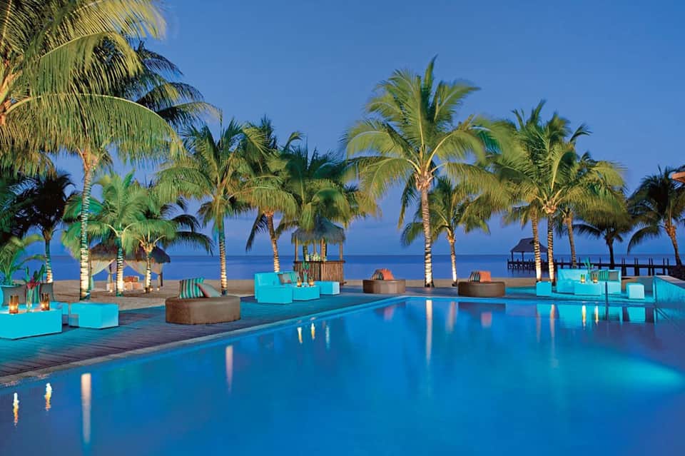 Beachfront infinity pool with palm trees, loungers, and turquoise ocean view at tropical resort