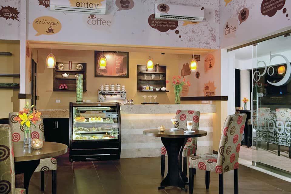 Warm coffee shop interior with cream walls, pendant lights, pastry display, and patterned seating