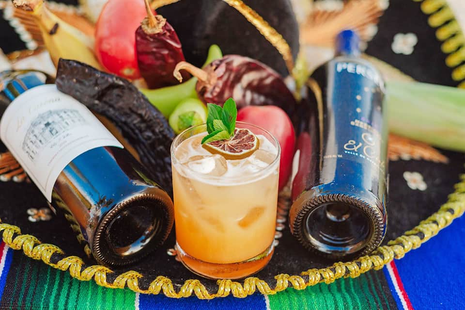 Craft cocktail with citrus garnish surrounded by premium spirits and fresh ingredients