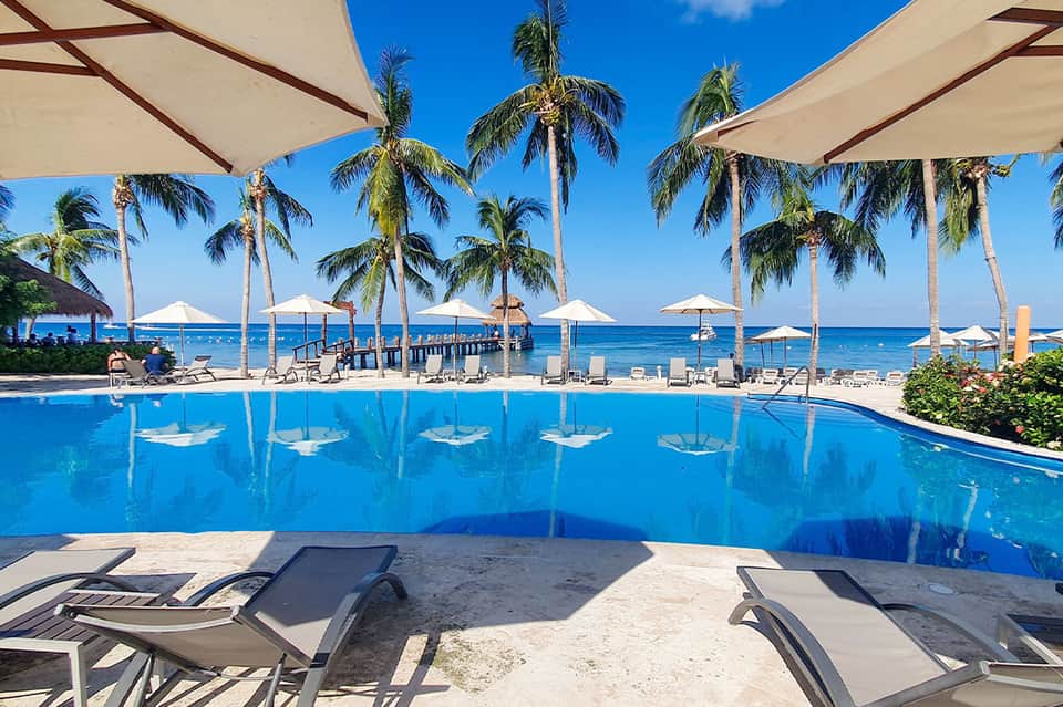 Resort infinity pool overlooking ocean with palm trees and beach umbrellas