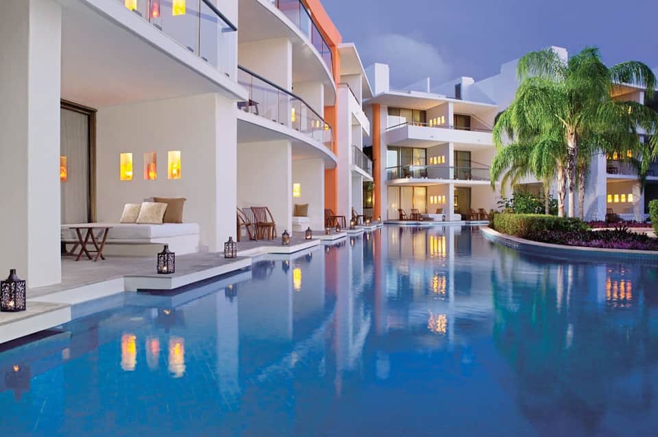 Elegant resort courtyard at dusk with infinity pool, palm trees, modern architecture, and ambient lighting
