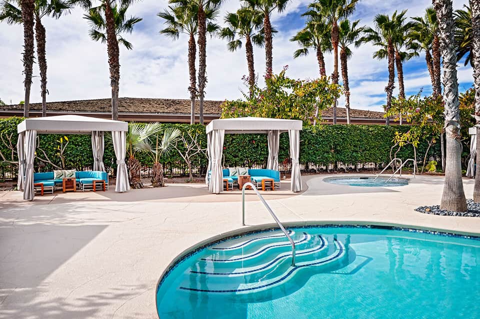 Resort pool deck with cabanas and palm trees under blue sky