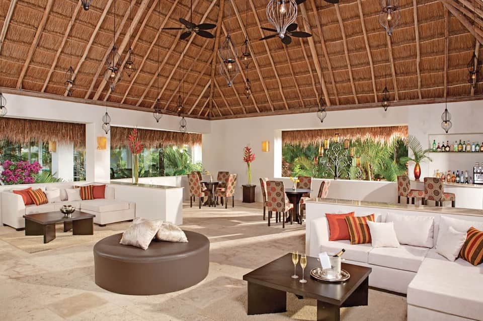 Elegant thatched-roof lounge with white furniture, tropical plants, and ocean views
