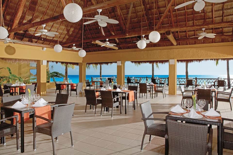 Beachfront restaurant with thatched roof, ceiling fans, and ocean views from open-air pavilion