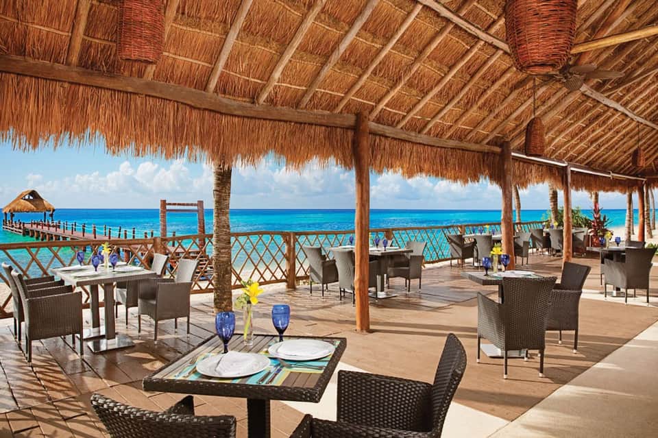 Beachfront dining pavilion with thatched roof, ocean views, and rattan furniture