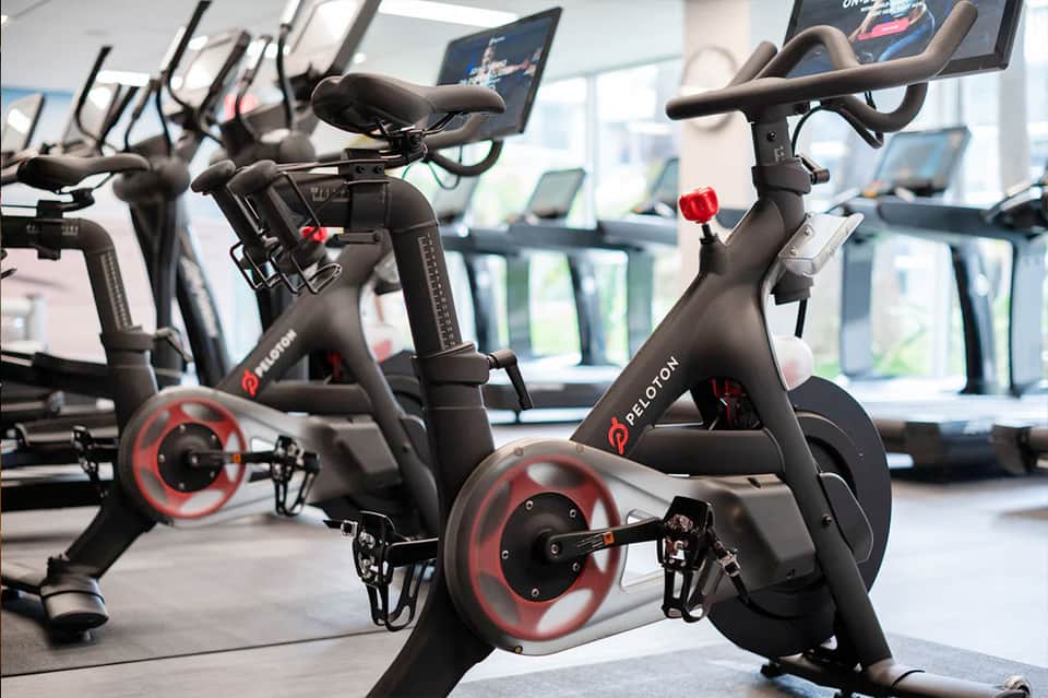 Row of black Peloton stationary bikes in bright fitness studio with windows