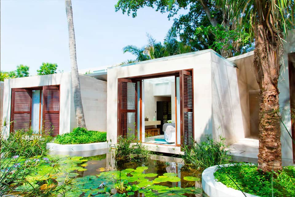 Modern spa bungalow with wooden louvers, stone walls, and surrounding water garden with lily pads