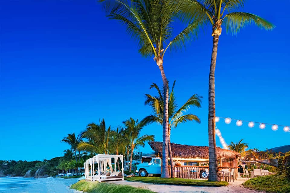Tropical resort venue with white gazebo, palm trees, vintage blue food truck, and beachfront setting