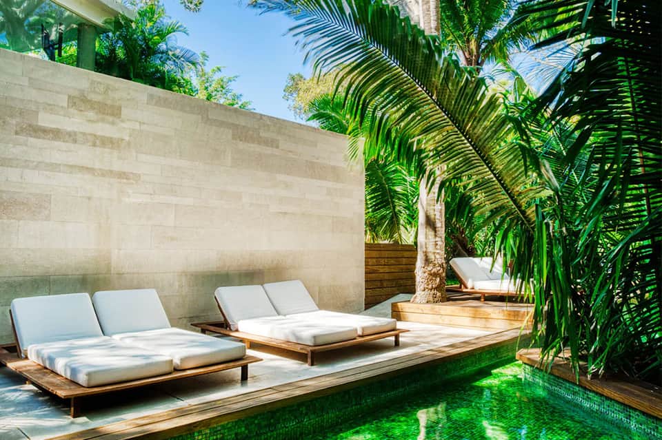 Spa-like courtyard with wooden loungers, white cushions, and lush tropical greenery and water feature