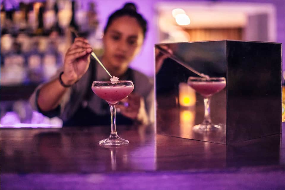 Bartender preparing pink cocktail with professional bar setup and purple ambient lighting