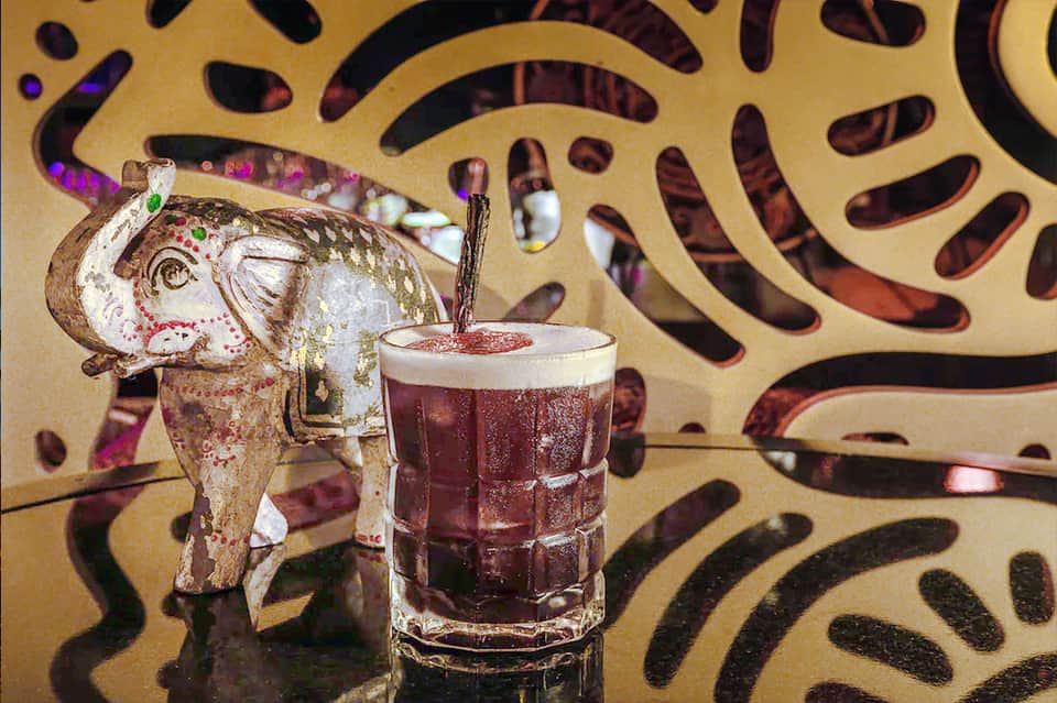 Decorative cocktail with tropical elephant figurine against patterned backdrop