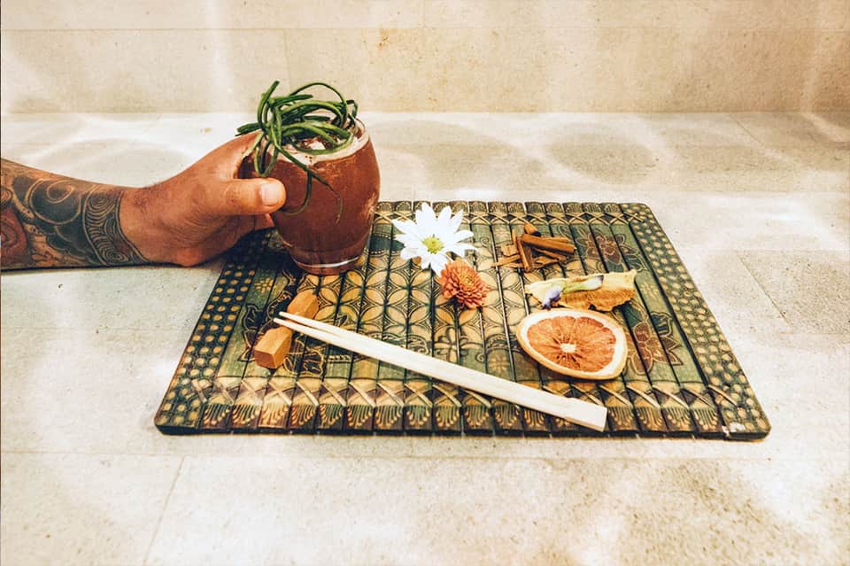 Craft cocktail with fresh herbs and garnishes on a decorative placemat with dried citrus