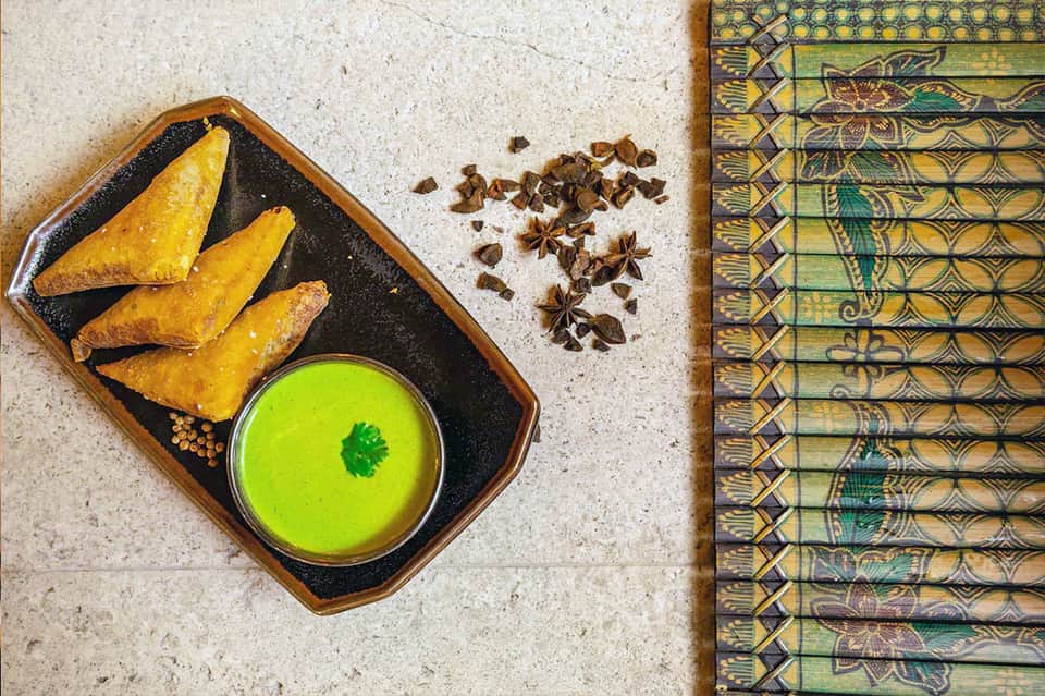 Golden samosas with green cilantro sauce and star anise spices on decorative placemat