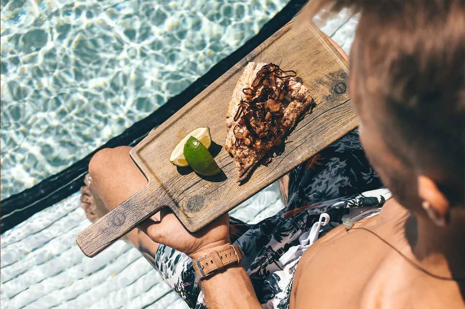 Person relaxing on overwater deck holding tray with chocolate treat and lime
