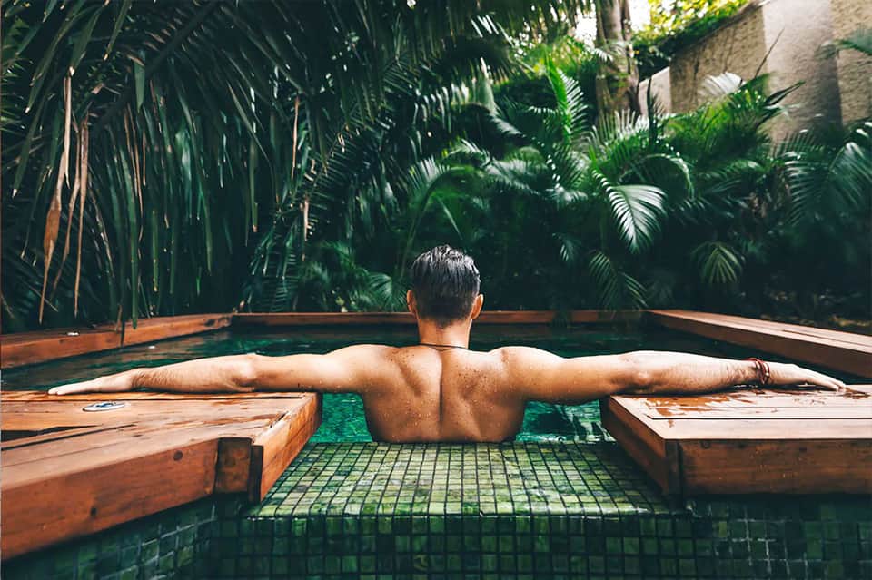Man relaxing in natural hot spring pool surrounded by tropical palm plants