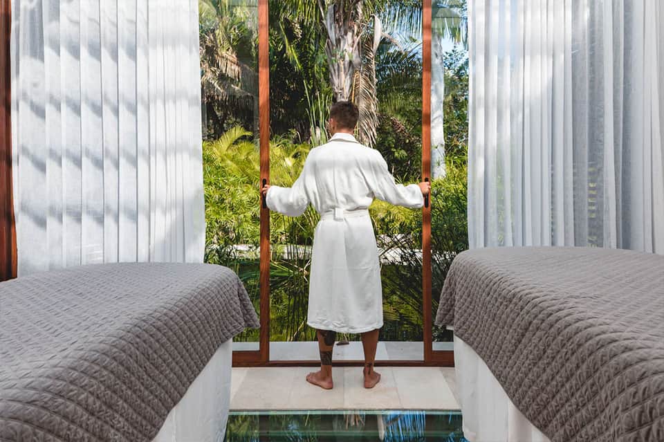 Man in white robe standing on terrace overlooking tropical garden and palm trees