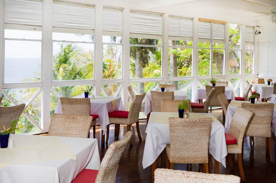 Waterfront dining room with wicker chairs, white tablecloths, and water views
